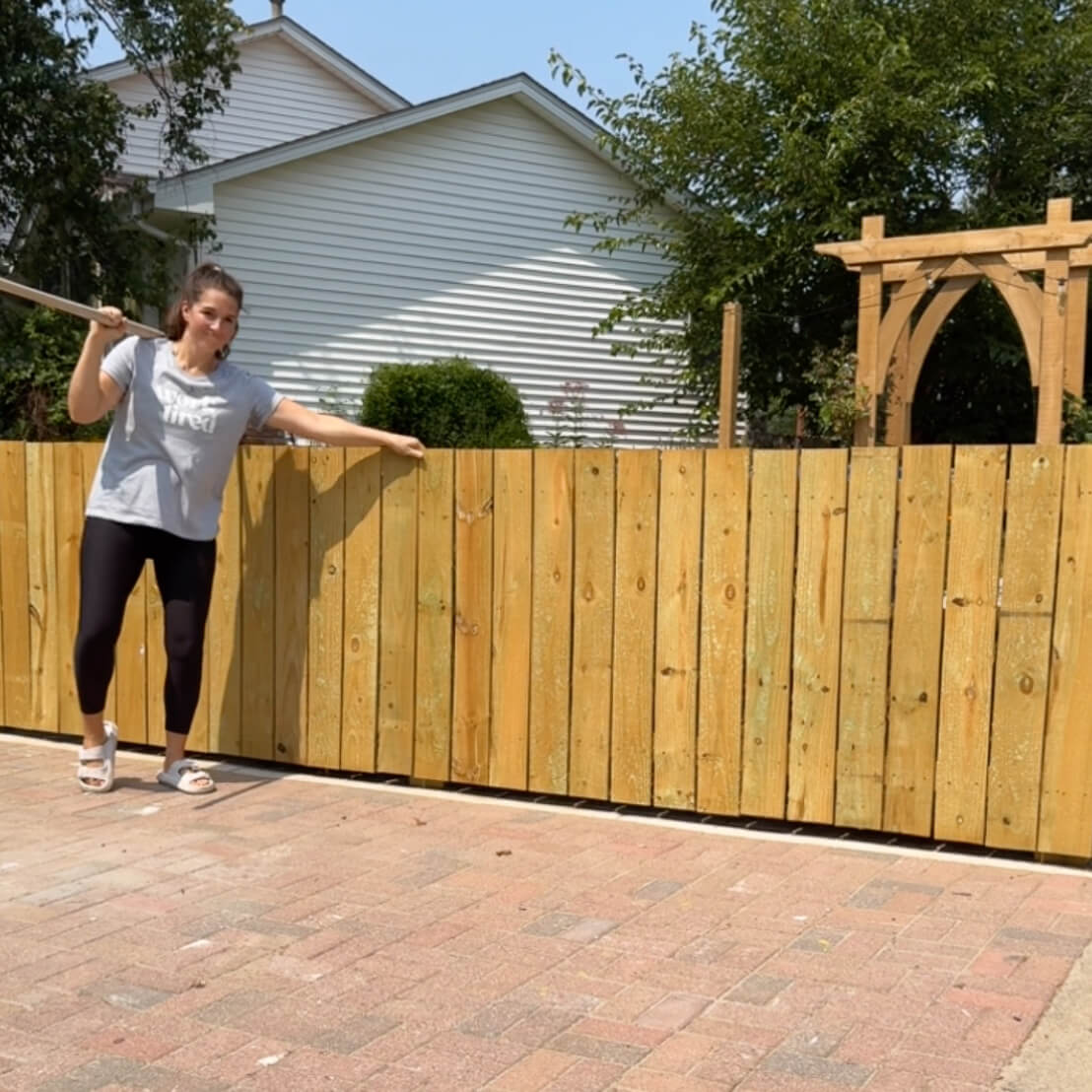 Completed wooden trash enclosure built on a herringbone brick pad with a decorative arbor in the background, perfect for outdoor bin storage.